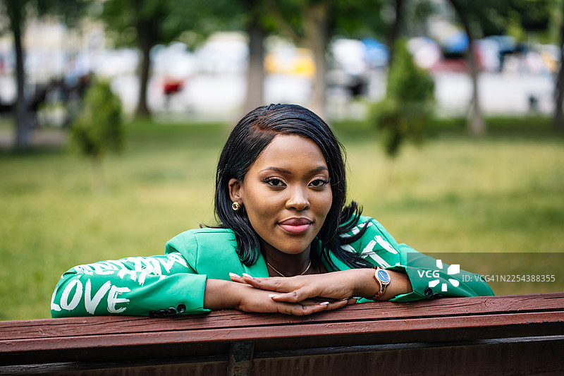 自信的女子身穿绿色西装外套，倚靠在公园长椅上的肖像照图片素材