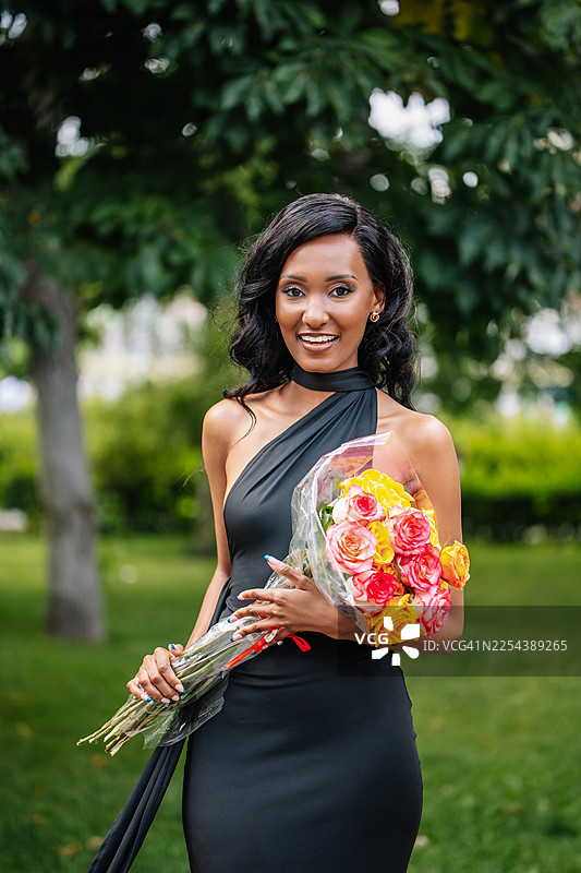 身着黑裙的优雅女士在公园手持鲜艳花束，准备庆祝图片素材