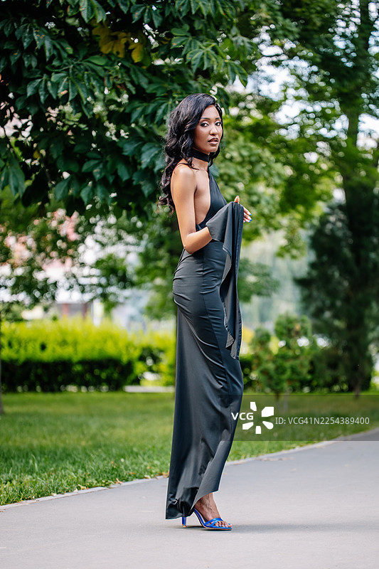 一位身着优雅黑色礼服的女士，在郁郁葱葱的绿色公园里优雅地摆姿势图片素材