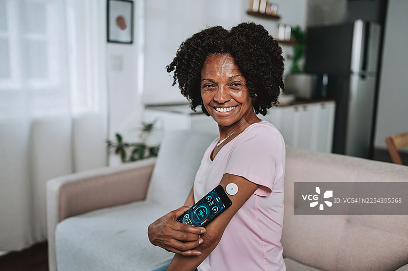一位快乐的年长黑人女性，看着镜头，扫描葡萄糖传感器图片素材