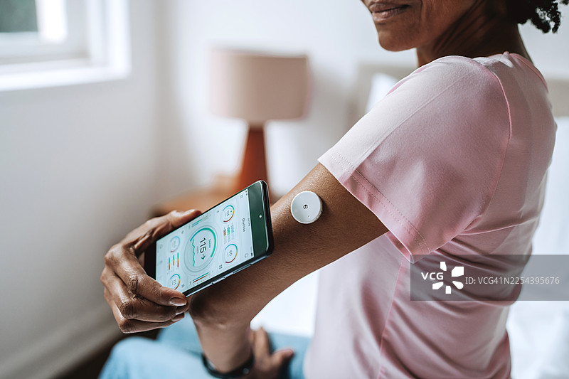 特写：老年黑人女性在床上用智能手机扫描葡萄糖传感器图片素材