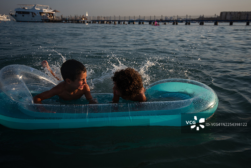 夕阳假期，两个帅气的男孩在充气船上嬉戏玩水。图片素材