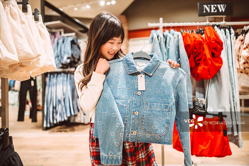 快乐的女孩在服装店挑选新的牛仔夹克图片素材