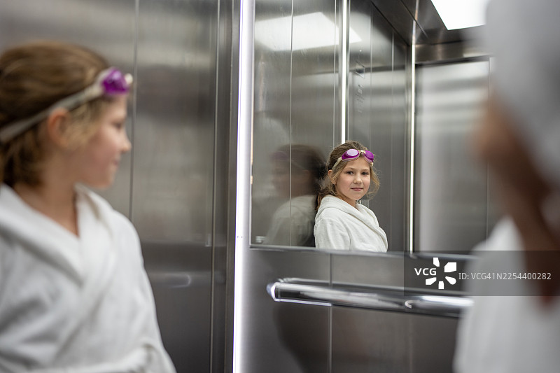 身穿白色长袍、戴着紫色护目镜的女孩在电梯镜子里看到了自己的倒影图片素材