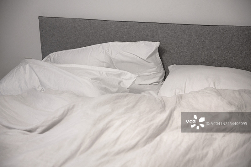凌乱卧室里未整理的床，铺着羽绒被套床罩图片素材