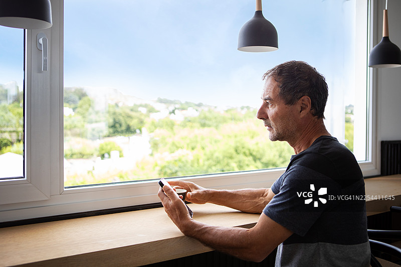 一名成年男子在咖啡馆靠窗使用他的智能手机图片素材