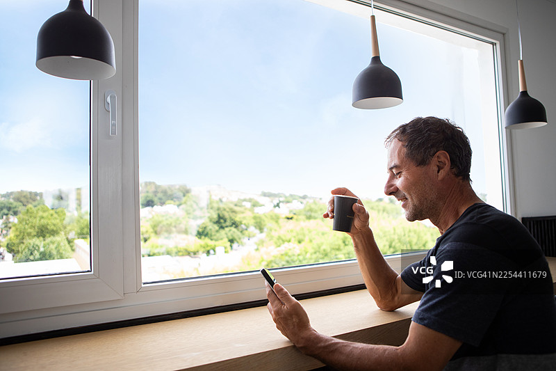 一名成年男子在咖啡馆靠窗使用智能手机图片素材