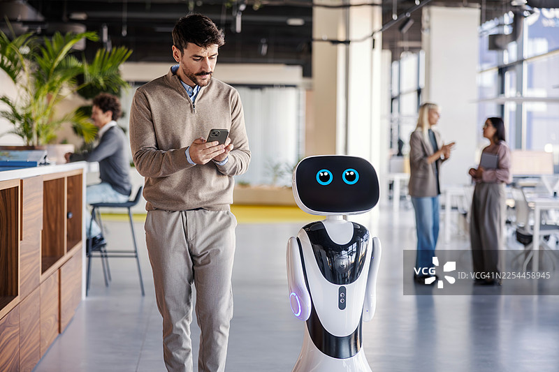 商务人士在办公室用智能手机与机器人互动图片素材