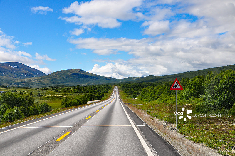夏季，公路穿过山地高原。有黄线和路牌。蓝天白云。图片素材