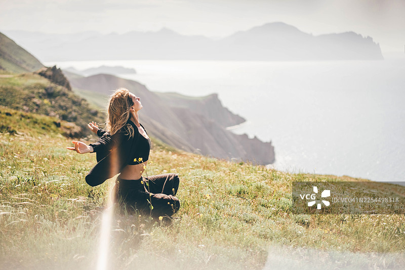 夕阳下，一位宁静的女子坐在岩石悬崖上冥想，远眺着无尽的大海和笼罩在薄雾中的群山。图片素材