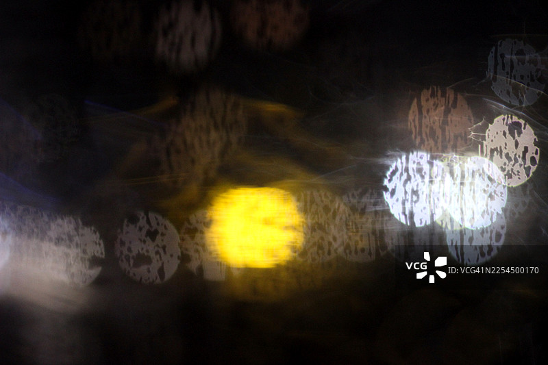 雨滴落在玻璃上，映衬着模糊的城市灯光图片素材