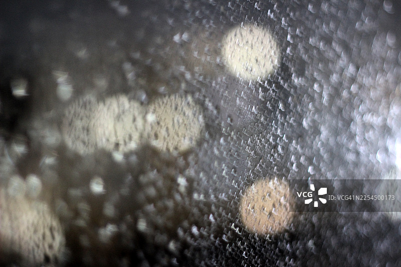 雨滴落在玻璃上，城市灯光模糊图片素材