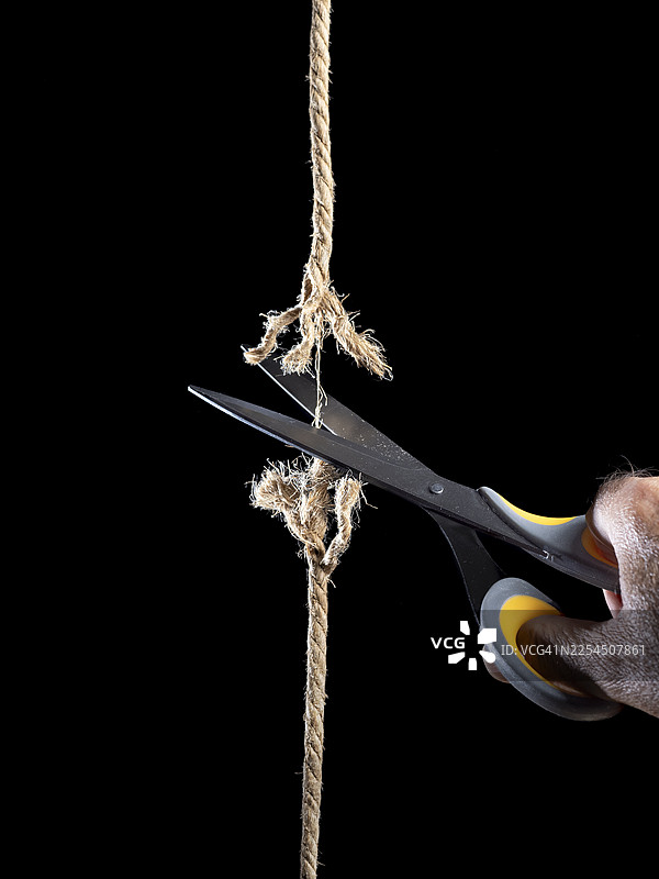 锋利的剪刀在黑色背景下剪断绳子。图片素材