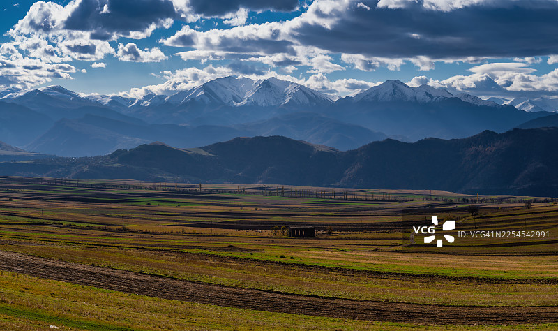 白雪皑皑的高加索山脉在亚美尼亚洛里省的农田上空，白天，戏剧性的云层笼罩着天空。图片素材
