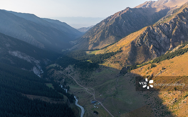 吉尔吉斯斯坦阿尔廷阿拉山谷的戏剧性黄金时刻景观，展示了蜿蜒的河流、茂密的松树林和巨大的天山雪峰。图片素材