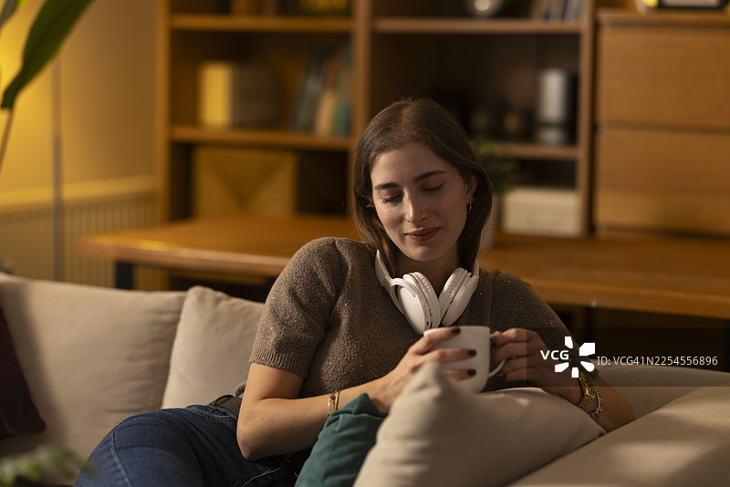 年轻女子在沙发上放松，喝着热饮图片素材