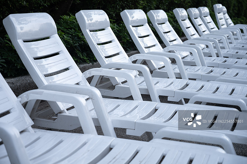 白色泳池椅整齐地排列在游泳池旁边。图片素材