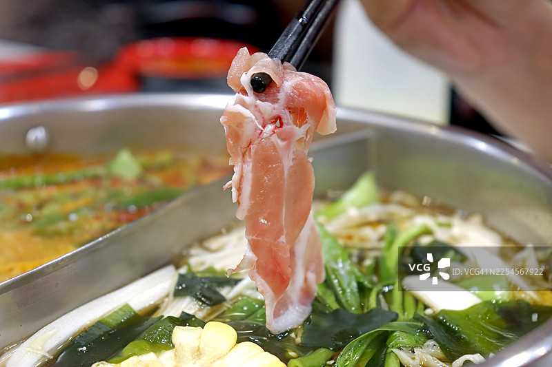 特写镜头：筷子夹着新鲜的薄切猪肉，放在沸腾的蔬菜涮涮锅上方图片素材