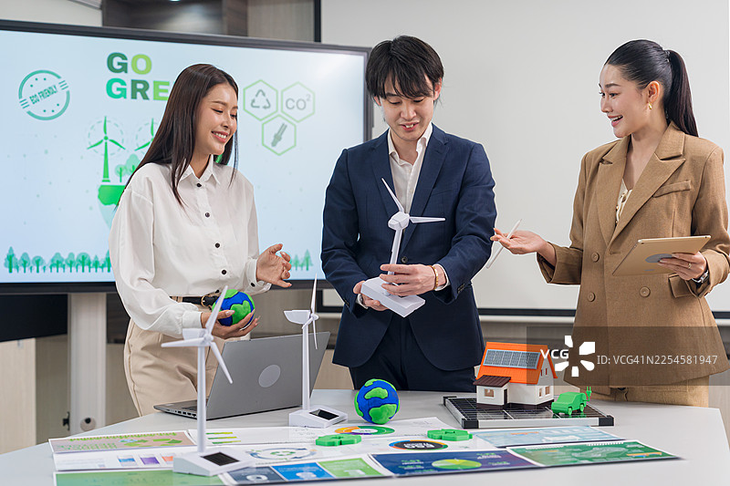 商业团队讨论可持续能源项目，背景中摆放着风力涡轮机模型。图片素材