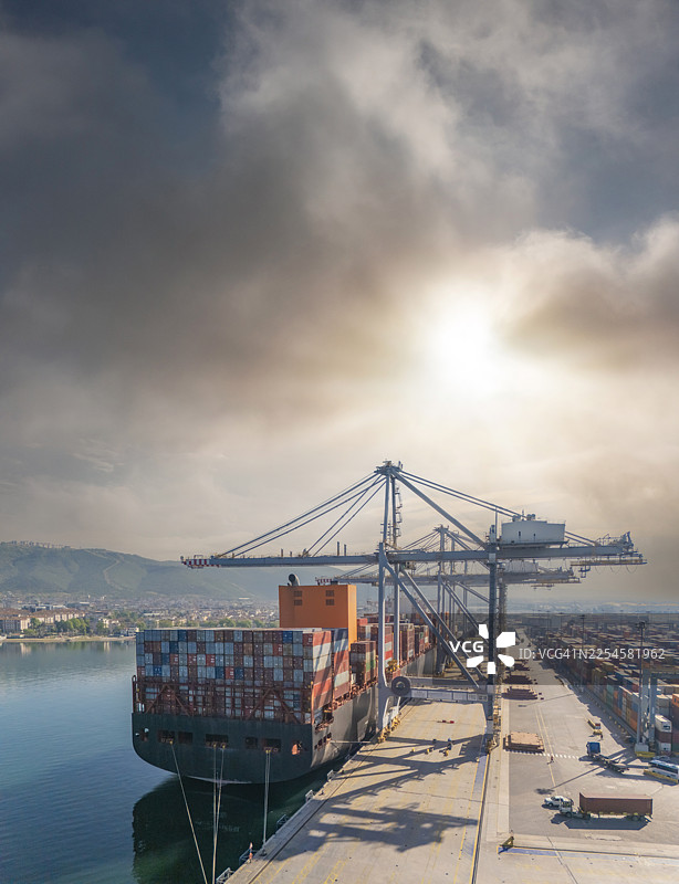 无人机视角拍摄，巨大的集装箱货轮装载着集装箱停靠在国际港口。图片素材