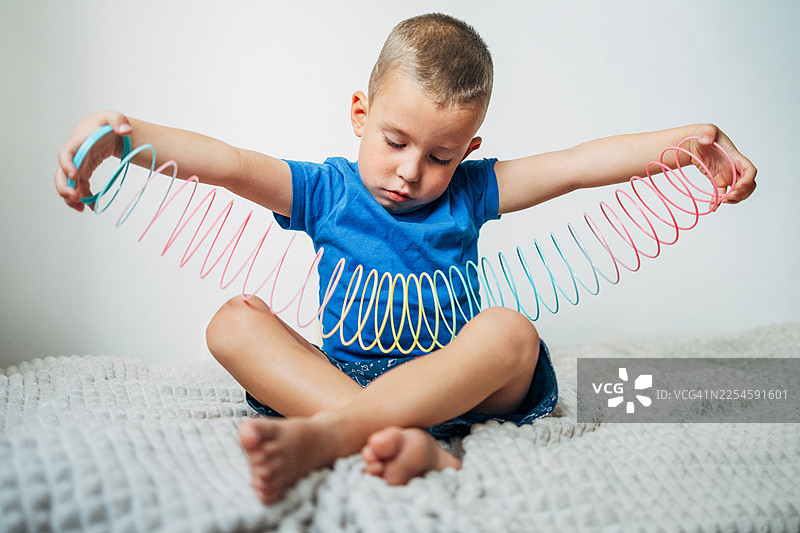 一个孩子坐在床上，专注地玩着一个彩色的伸缩玩具图片素材