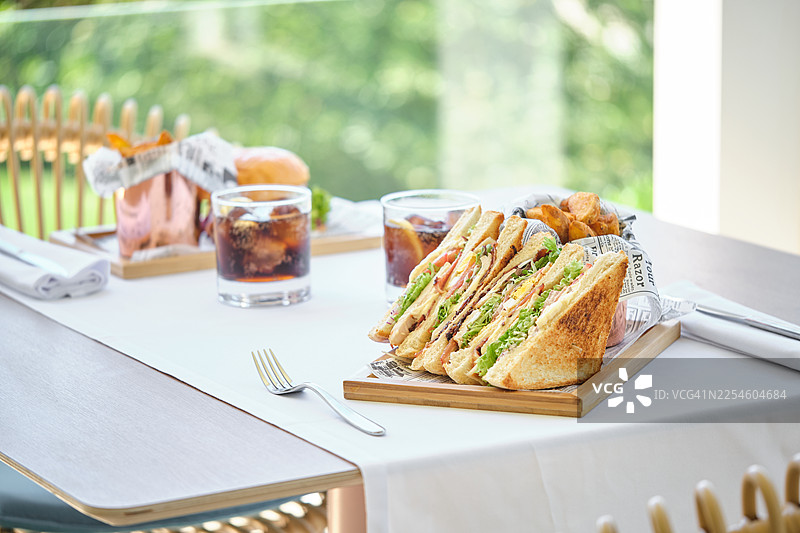 户外餐桌上供应的俱乐部三明治和可乐图片素材