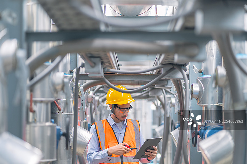 身着安全帽和背心的工程师正在对机械进行检查，利用先进技术进行高效的工业运营分析。图片素材