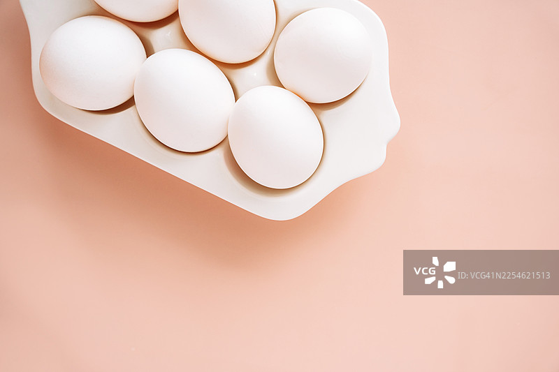 俯视视角，浅桃粉色背景下的鸡蛋托盘里的白色鸡蛋，留有复制空间图片素材