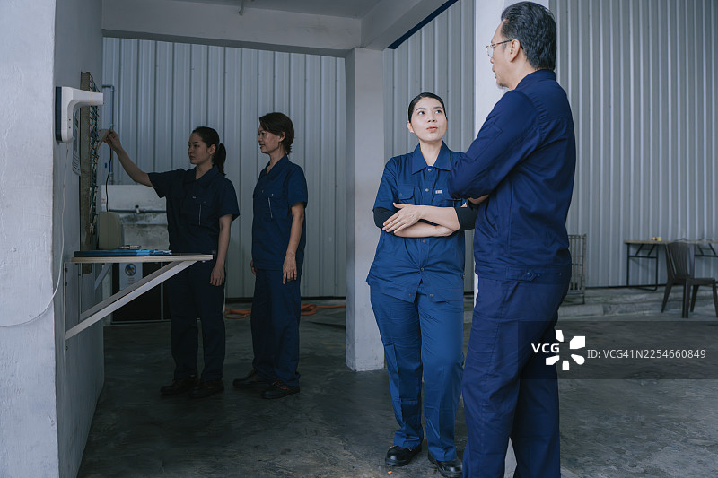 亚洲男性工厂工人与亚裔女同事交谈，同时亚裔女工在打卡机上打卡图片素材