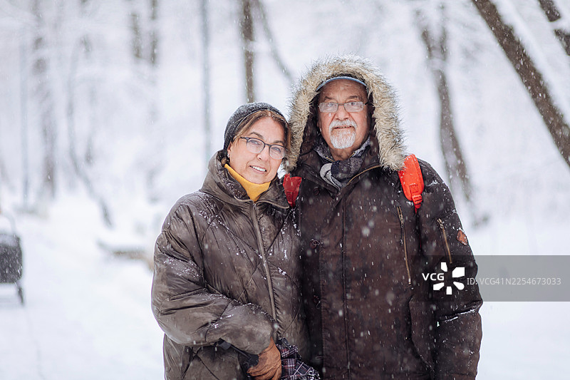 一对年迈的夫妇在雪后的冬季公园里拥抱，一同享受寒冷的天气图片素材