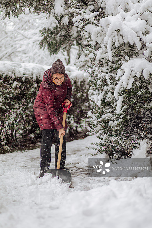 一位年长的女性在冬日降雪中清理人行道上的积雪图片素材