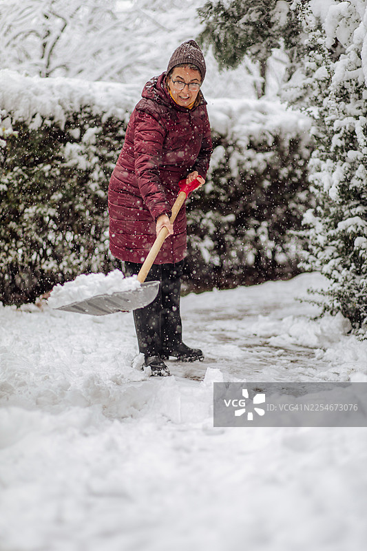 一位女士在冬季仙境中铲雪，清理户外的雪道图片素材