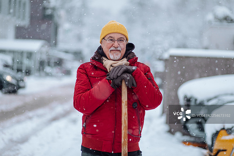 一位身穿红色夹克的年长男子，在雪中手持铁锹准备铲雪图片素材