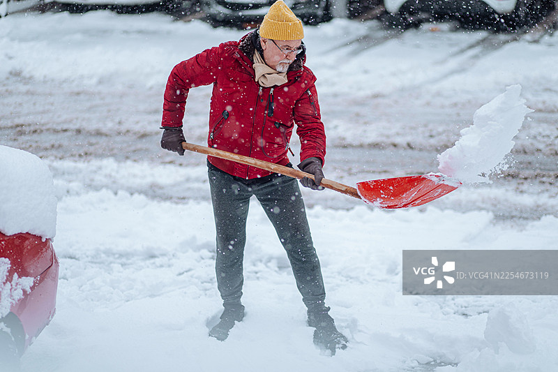 一位老人穿着红色夹克，在寒冷的冬日铲雪图片素材