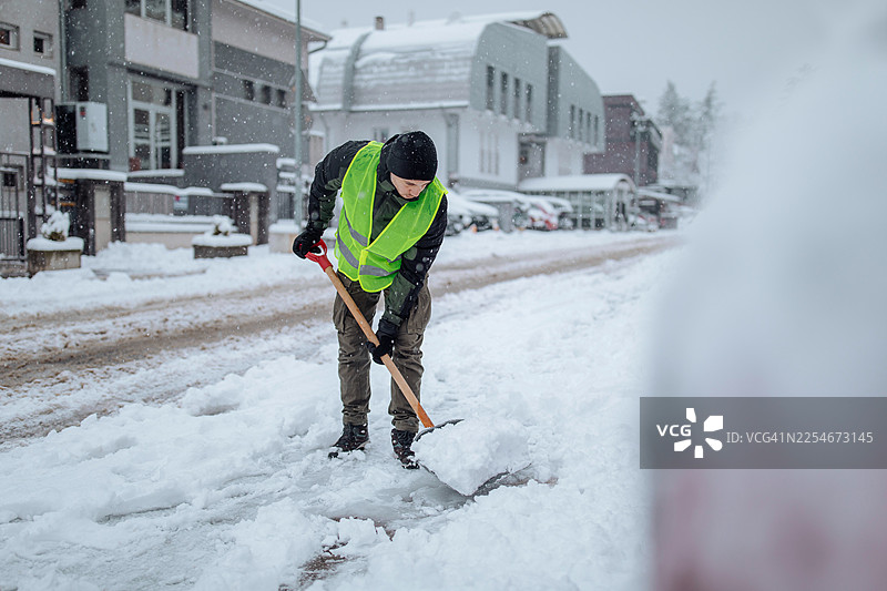 一名穿着高能见度背心的男子在冬季风暴中清理街道积雪图片素材