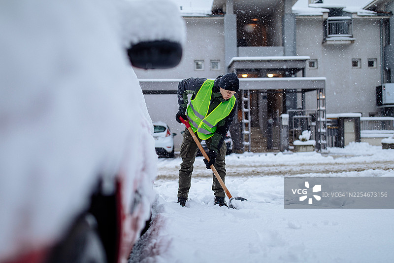 一名穿着高可见度背心的男子在下雪天于房屋前铲雪图片素材