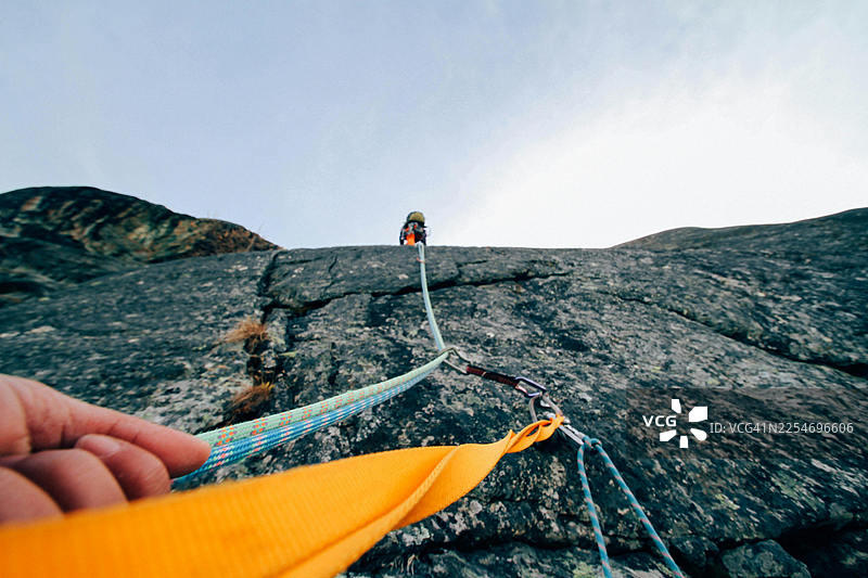 攀岩者的一只手握着安全绳，另一名攀岩者正朝着明亮的天空攀登岩壁图片素材