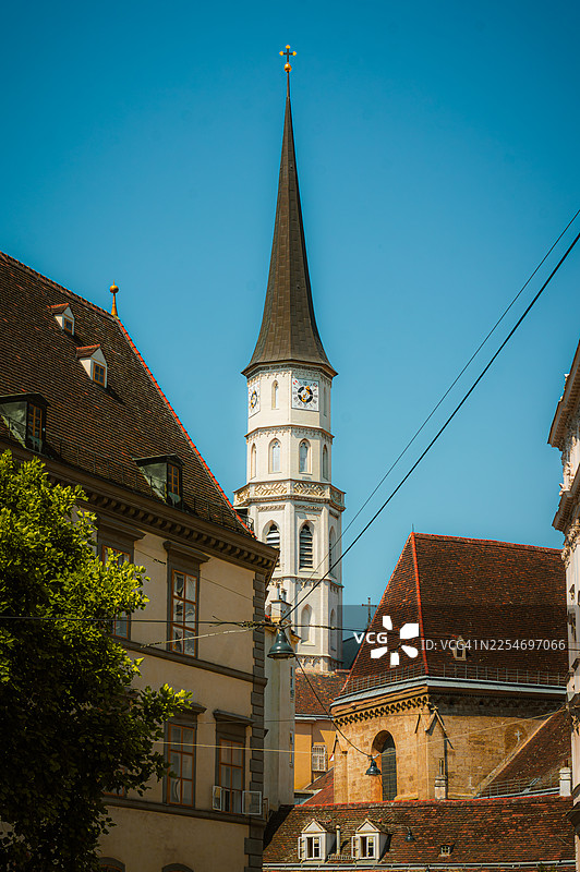 从低角度拍摄的历史悠久的教堂尖顶和钟楼，周围是传统欧洲建筑，在晴朗的蓝天下，维也纳，奥地利，圣米歇尔堂图片素材