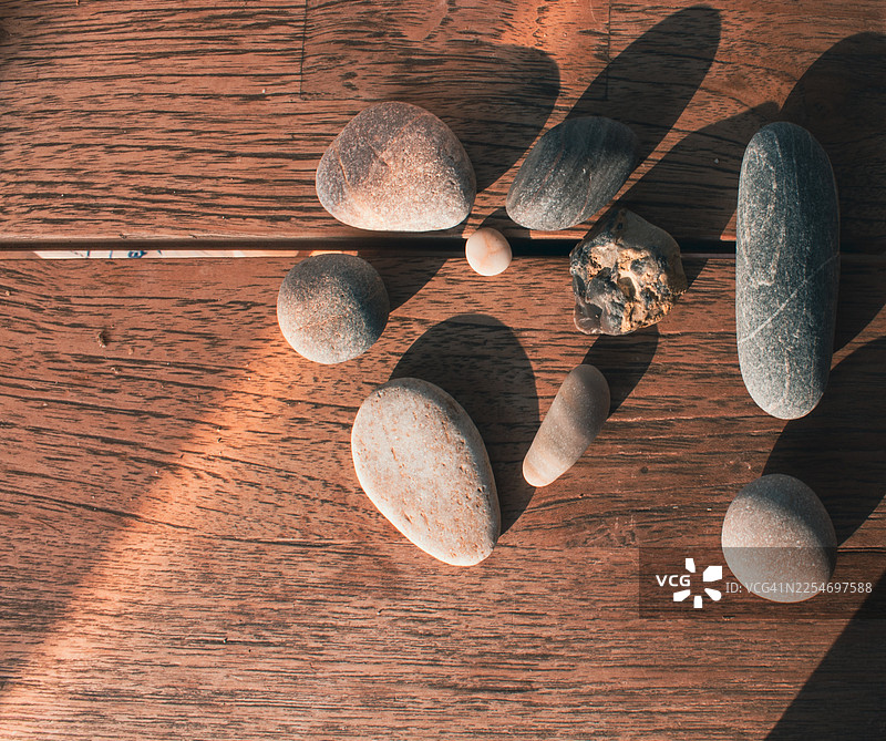 质朴的木桌上，光滑的河石和卵石呈圆形排列，沐浴在自然阳光下图片素材