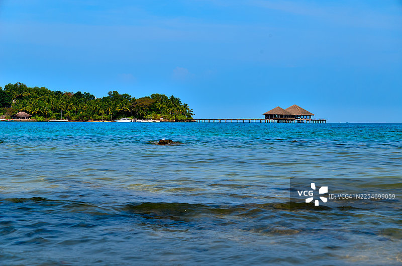 柬埔寨戈公岛，宁静的热带海景，远处有水上平房和郁郁葱葱的岛屿，天空湛蓝图片素材