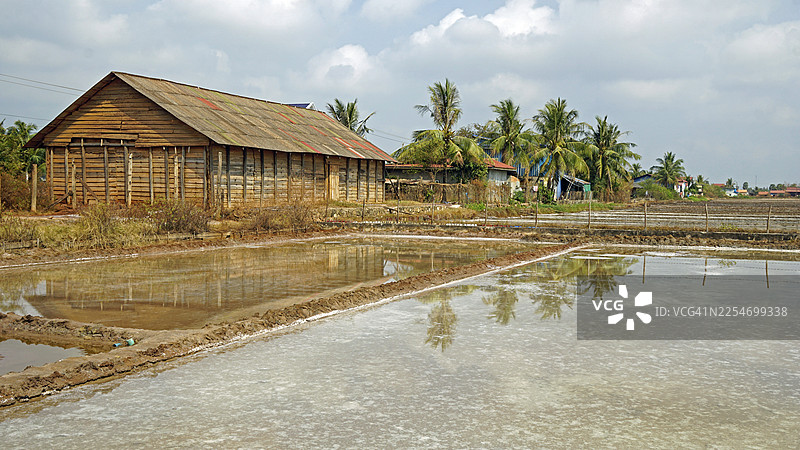 柬埔寨乡村风光中，传统木制建筑旁是盐田，天空多云图片素材