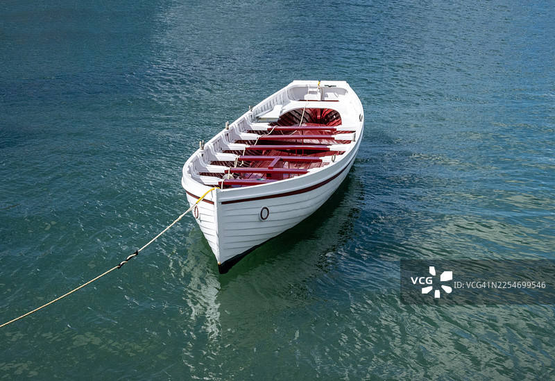 从高处俯瞰，一只红白相间的划艇漂浮在平静的蓝绿色水面上，用绳子拴着。图片素材