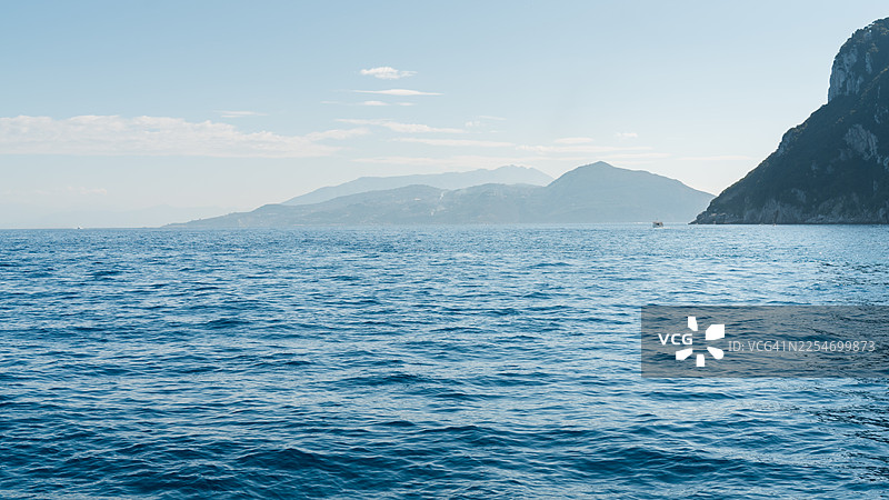 晴朗天空下，辽阔的蓝色大海与远山构成的风景图片素材