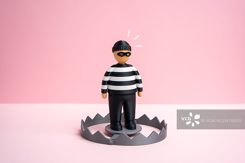 一个强盗玩偶摇摇欲坠地站在捕兽夹上，象征着粉色背景下的风险与危险图片素材