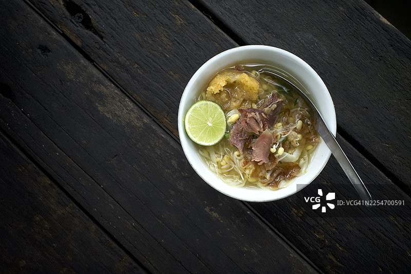 俯视一碗盛在深色木桌上的美味面汤，配有青柠和肉图片素材