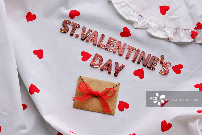 从高处看“圣瓦伦丁节”文字，搭配红心和礼物信封，背景为白色织物图片素材