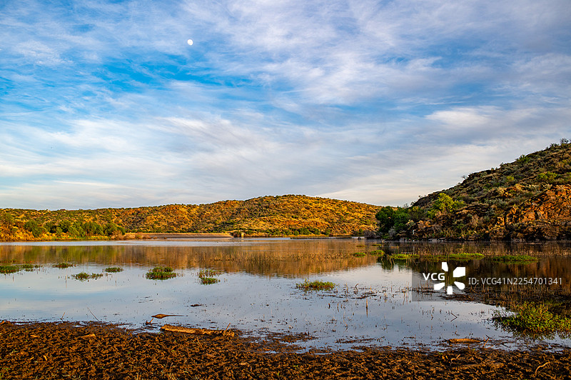 纳米比亚，纳马比兰，湖泊宁静的风景倒映着蔚蓝的天空，点缀着几朵云彩，远处是连绵的山丘，一轮明月可见图片素材