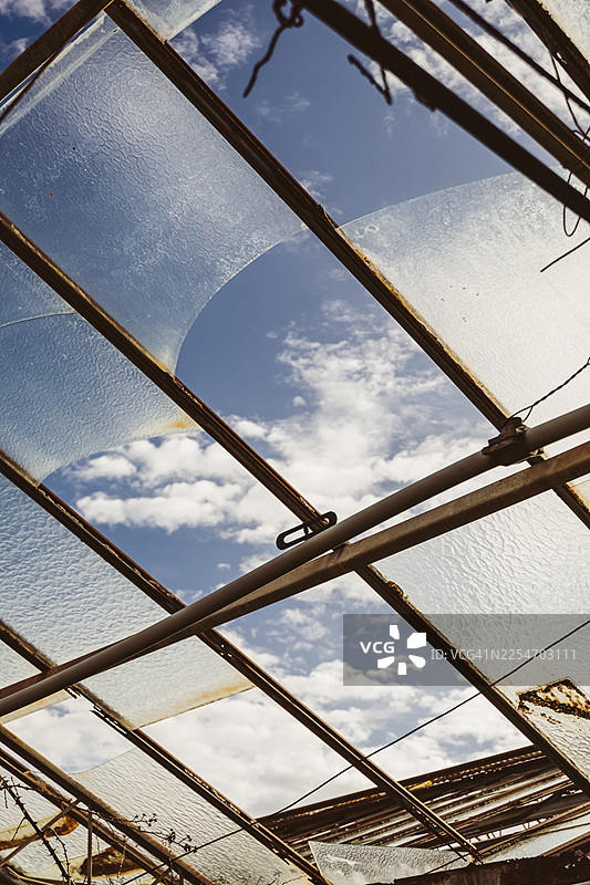 从低角度拍摄的破损玻璃屋顶，背景是蓝天白云，展现出荒废和失修的状态，地点：意大利米拉佐图片素材