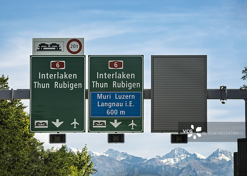 瑞士高速公路上指示城市和绕行的交通标志，背景是白雪皑皑的阿尔卑斯山，因特拉肯。图片素材
