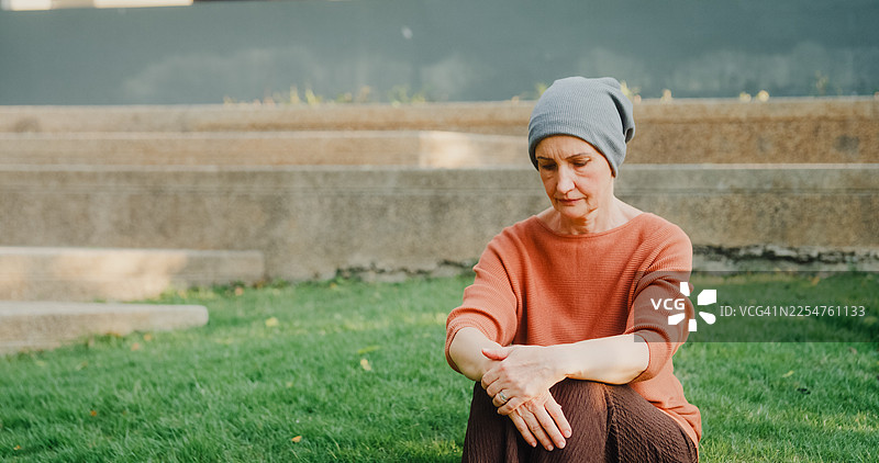 一位戴着头巾的年长女性癌症患者，在公园里独自静思，庆祝康复。癌症生存概念。图片素材